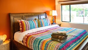 A bed with a colorful blanket and pillows, a bedside lamp, and a window with a view of trees. - Eclectic boho style apartment in the heart of West Sedona (Sedona)