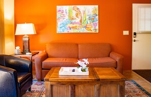 Un salon avec un canapé, une table basse, une lampe et un tableau coloré accroché au mur.