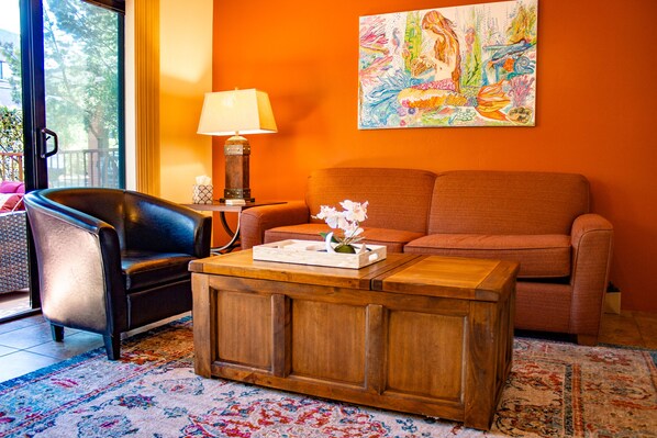 Un salon avec un fauteuil en cuir noir, un canapé orange, une table basse en bois et une lampe.