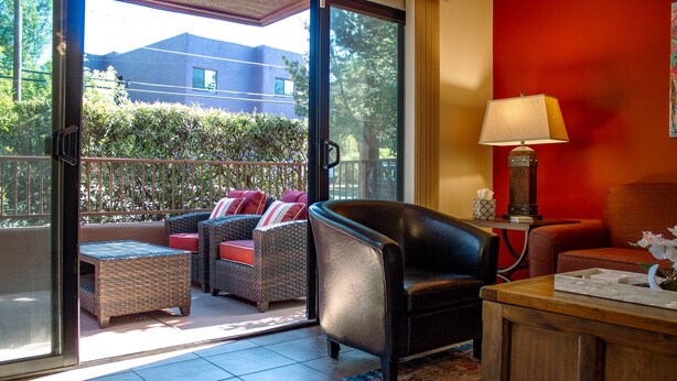 A room with a sliding glass door leading to a balcony, wicker furniture, a leather armchair, a wooden side table with a lamp, and a small table with a vase. - Eclectic boho style apartment in the heart of West Sedona (Sedona)