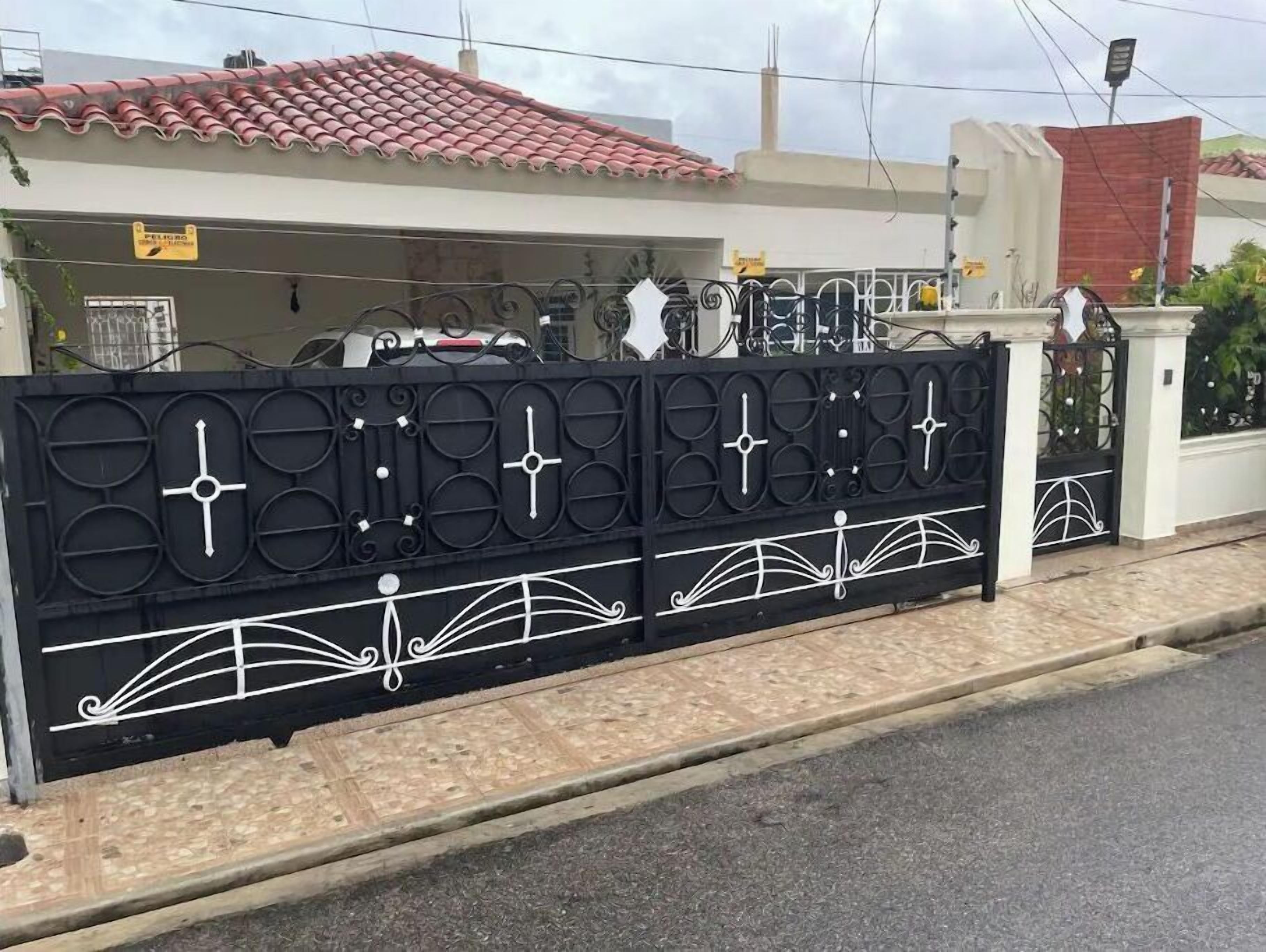 Propiedad amurallada con una cerca metálica decorativa que presenta diseños geométricos y un portón blanco.