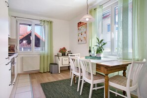 Un comedor con una mesa de madera y sillas blancas, un radiador, una ventana con cortinas y un cartel en la pared.