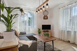 A modern living room with a sofa, a coffee table, a TV, and a potted plant. - Dog-Friendly Apartment Haus Rosi with Shared Garden & Wi-Fi (Friedrichshafen)
