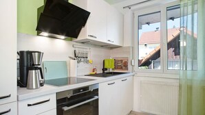 Une cuisine avec des meubles blancs, une hotte noire, une machine à café et une fenêtre donnant sur des immeubles.