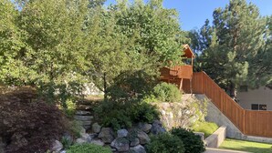 Ein Garten mit einer Holzterrasse, einer Steinmauer und einer Terrasse mit Gartenmöbeln.