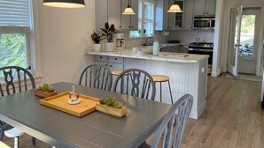A modern kitchen with white cabinets, a central island, pendant lighting, and a dining area with a gray table and chairs. - Charming spacious 1933 newly renovated private home. Walk to trails (Highlands)