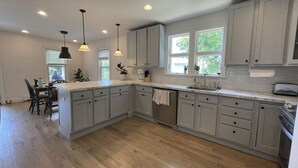 A modern kitchen with grey cabinets, a central island, pendant lights, and a view of the outdoors through windows. - Charming spacious 1933 newly renovated private home. Walk to trails (Highlands)