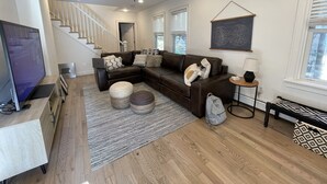 A modern living room with a sectional sofa, a flat-screen TV, a ceiling fan, and a staircase leading to another level. - Charming spacious 1933 newly renovated private home. Walk to trails (Highlands)