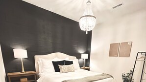 Une chambre à coucher avec un grand lit, deux tables de chevet avec des lampes, un lustre, une lampe sur pied, une petite plante et un tapis.