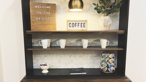 Un coin café en bois, agrémenté d’une pancarte indiquant « BIENVENUE AU HEIGHTS COFFEE », d’une étagère avec des tasses blanches, d’un bol rempli de collations, d’un livre et d’un porte-bouteilles décoratif.