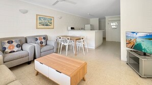 Una sala de estar moderna con sofá, mesa de centro, televisor, comedor, cocina y ventilador de techo.