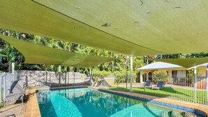 Una piscina con cubierta de madera, zona sombreada y jardín cercado.