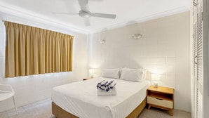 Un dormitorio con cama, mesita de noche y ventilador de techo, además de una ventana con cortinas.