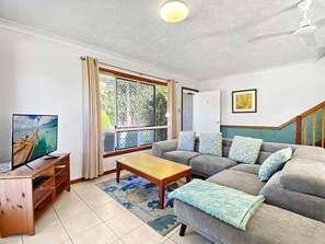 Ein Wohnzimmer mit einer Couch, einem Couchtisch, einem Fernseher auf einem Holzboden und einem Fenster mit Vorhängen.