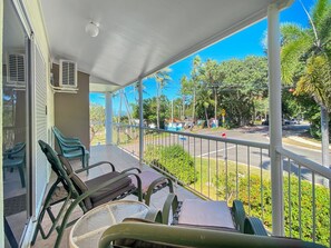 Een balkon met stoelen en een tafel, uitkijkend op een straat met palmbomen en een heldere lucht.