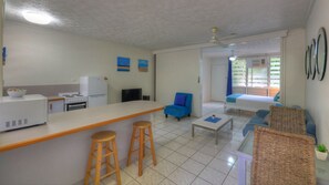 A compact hotel room with a kitchenette, a dining area, a living space with a sofa and armchairs, and a balcony with a view.