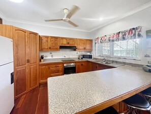 A kitchen with wooden cabinets, a granite countertop, a microwave, and a ceiling fan.