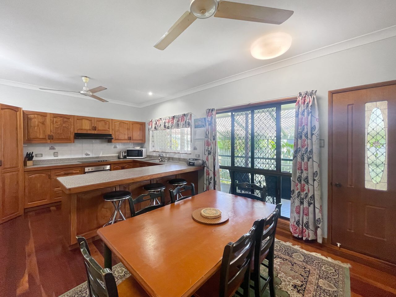 A kitchen with wooden cabinets, a dining table, bar stools, and a ceiling fan.