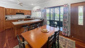 A kitchen with wooden cabinets, a dining table, bar stools, and a ceiling fan. - Arcadia Gardens (Arcadia)