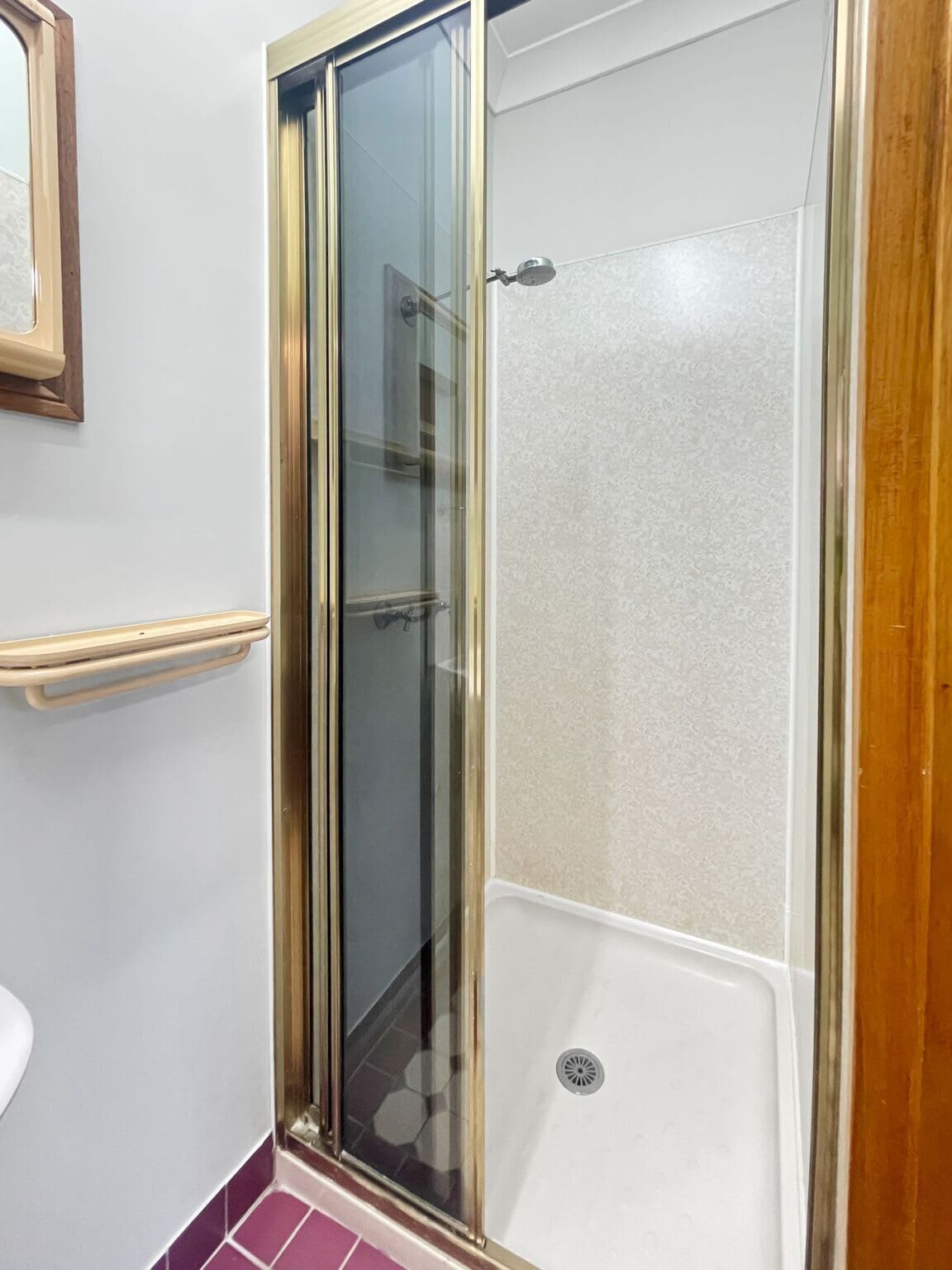 A shower with a glass door, a wooden frame, and a white tiled wall.