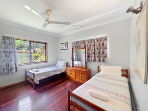 A bedroom with two single beds, a wooden dresser, a ceiling fan, and a window with curtains.