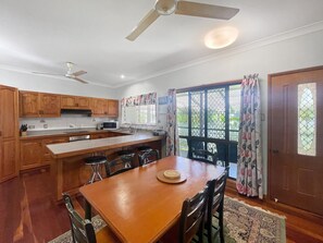 A kitchen with wooden cabinets, a dining table, bar stools, and a ceiling fan.