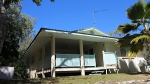 Einbungalow mit Veranda, Satellitenschüssel und Palmenbaum.