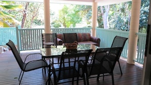 A covered outdoor seating area with a table and chairs, a patterned sofa, and a view of trees. - Lana's Cottage (Arcadia)