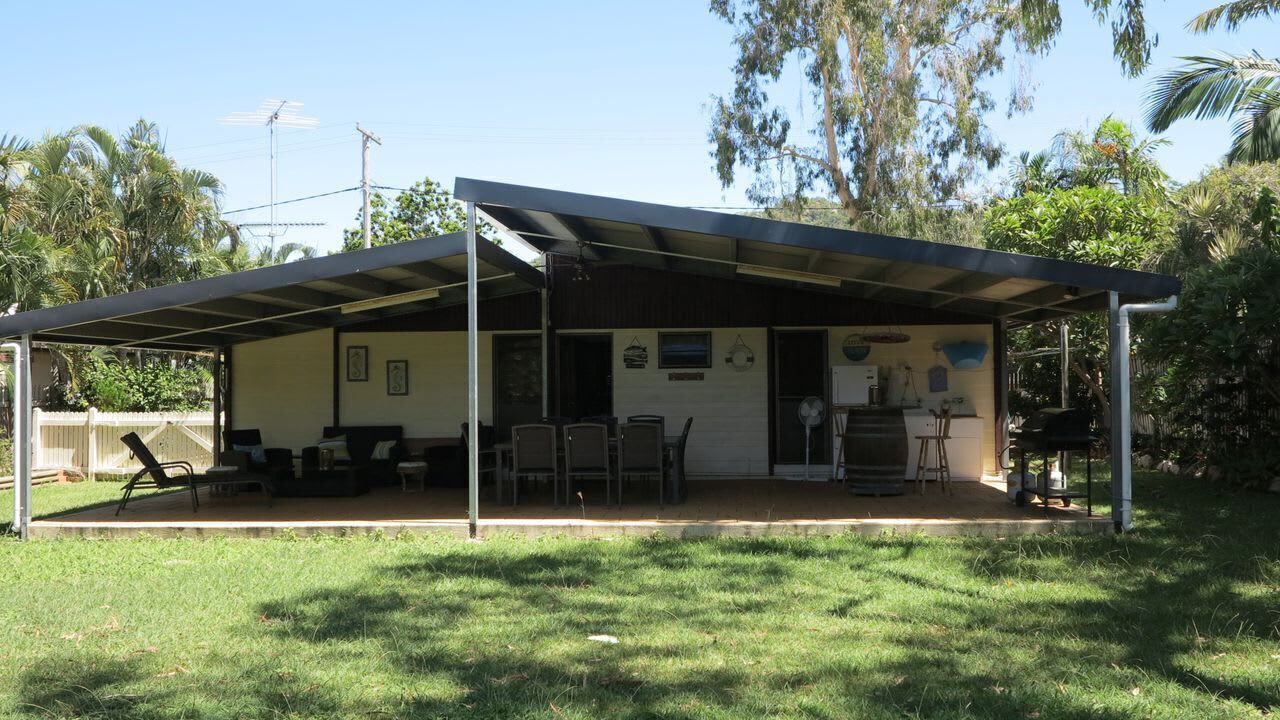 Un espace extérieur abrité, équipé de chaises et de tables, une petite scène et un bâtiment doté d’un toit plat et de fenêtres.