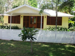 A yellow house with a white picket fence, a small tree in the front yard, and a porch with a ceiling fan. - Lemonade (Arcadia)