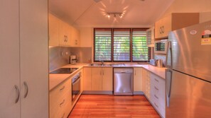 A modern kitchen with wooden cabinets, stainless steel appliances, and a window with blinds. - Lemonade (Arcadia)