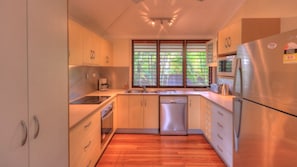 A modern kitchen with wooden cabinets, stainless steel appliances, and a window with blinds. - Lemonade (Arcadia)