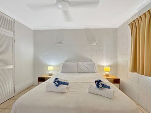 A hotel room with a large bed, two bedside tables with lamps, a ceiling fan, and a window with curtains.
