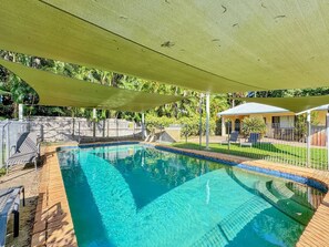 A swimming pool with a wooden deck, a shaded area, and a fenced garden.