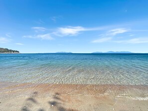 A beach with clear water, a sandy shore, and distant mountains.