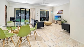 Ein modernes Wohnzimmer mit einem Glastisch, grünen Stühlen, einer Couch, einem Fernseher und einem Balkon mit Blick.