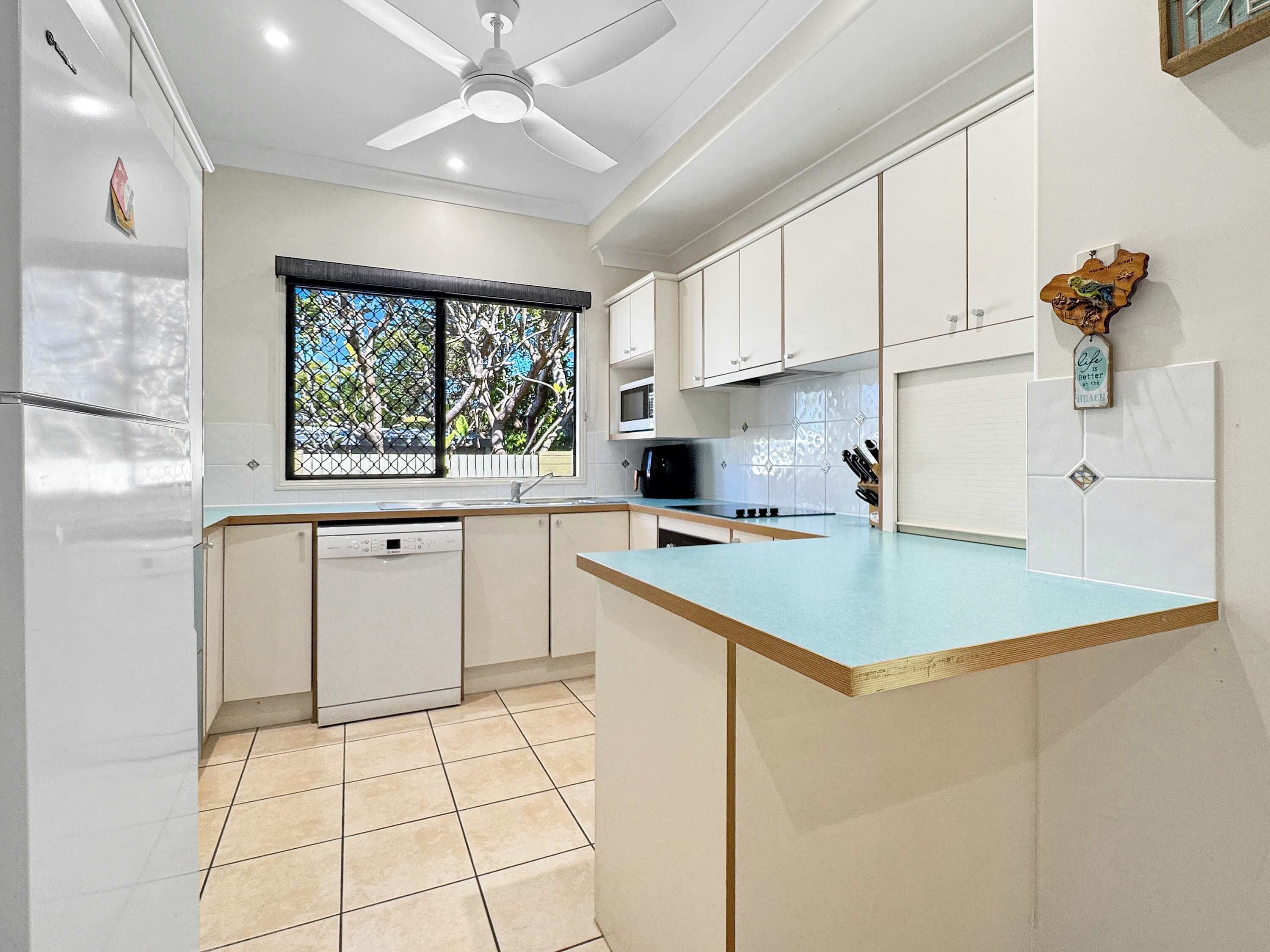 A modern kitchen with white cabinets, a blue countertop, a built-in microwave, and a ceiling fan.