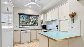 A modern kitchen with white cabinets, a blue countertop, a built-in microwave, and a ceiling fan.