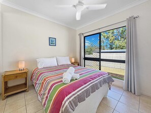 A hotel room with a bed, a nightstand, a ceiling fan, a window with curtains, and a view of the outside. - Arcadia Villa 3 (Arcadia)