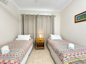 Quarto de hotel com duas camas, uma mesa de cabeceira com abajur e um quadro na parede.