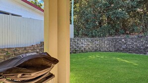 Eine Terrasse mit Grill, einer Steinsäule und einem gepflegten Rasen.