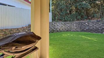 A patio area with a grill, a stone wall, and a well-maintained lawn.