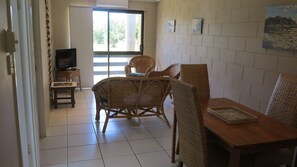 A room with a dining table, wicker chairs, a television on a stand, and a view through a sliding door. - Casual Lodge Unit 4 short walk to Nelly Bay Beach (Nelly Bay)