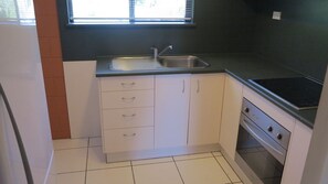 A compact kitchen with white cabinets, a stainless steel sink, and a built-in oven. - Casual Lodge Unit 4 short walk to Nelly Bay Beach (Nelly Bay)
