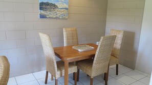 A dining table with four chairs, a painting on the wall, and a tiled floor.