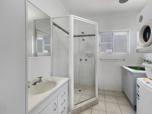 A bathroom with a glass-enclosed shower, a sink with a mirror, and a washing machine. - Arcadia Beach Unit 4 (Arcadia)