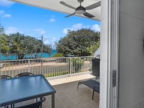 A balcony with a table and chairs, a ceiling fan, and a view of a swimming pool and trees.