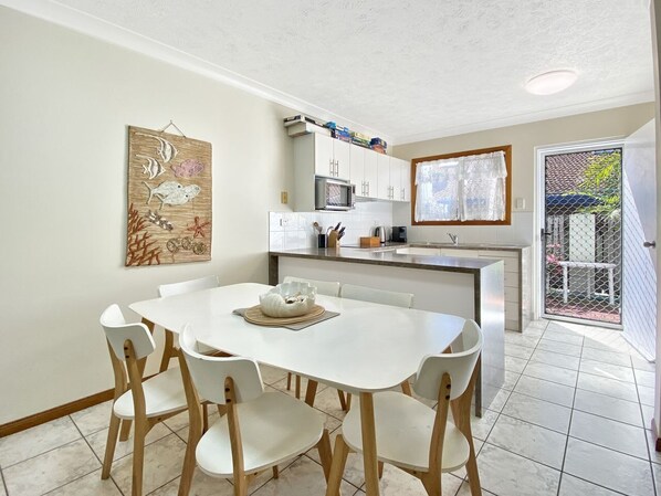 A kitchen with white cabinets, a microwave, and a dining area with a white table and chairs. - Island Magic Townhouse 5 (Arcadia)