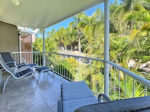A balcony with two lounge chairs and a view of palm trees.