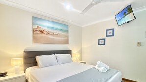 A neatly arranged bedroom with a bed, bedside lamps, a ceiling fan, a mounted TV, and a beach-themed painting. - Island Magic Townhouse 5 (Arcadia)